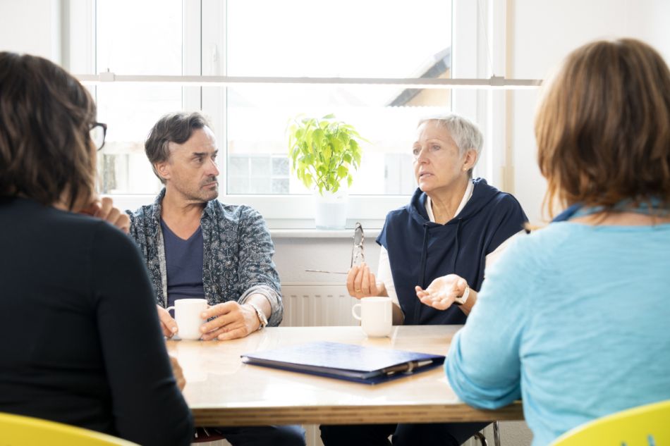 4 Krebspatienten einer Selbsthilfegruppe sitzen am Tisch und reden
