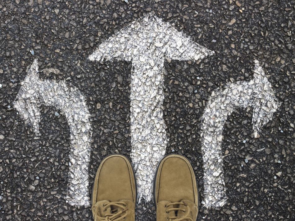 Zwei Schuhe stehen vor verschiedenen Richtungspfeilen auf einer Straße