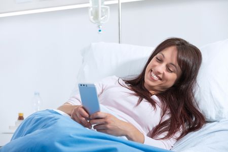 Junge Frau chattet im Krankenhausbett.