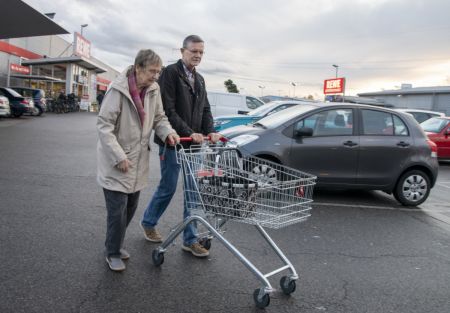 Ältere Dame und ein Mann schieben einen Einkaufswagen über einen Supermarkt-Parkplatz