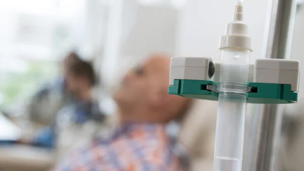 Tropf, © Krebsinformationsdienst, DKFZ; Foto: Tobias Schwerdt Ein Tropf im Vordergrund, im Hintergrund ist verschwommen ein Mann zu sehen.