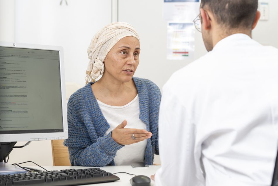 Krebspatientin mit Kopftuch spricht mit einem Arzt