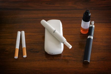 Foto von Zigaretten, einem Tabakerhitzer mit eingestecktem Tabakstick und einer E-Zigarette mit Nachfüllpack