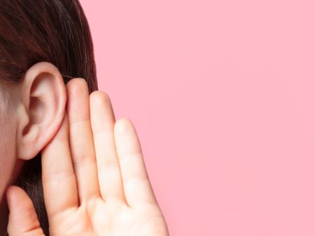 Eine Person hält ihre Handfläche hinter das Ohr, um besser zu hören.