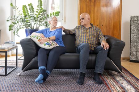 Älteres Paar sitzt auf einer Couch, er legt ihr tröstend die Hand auf die Schulter