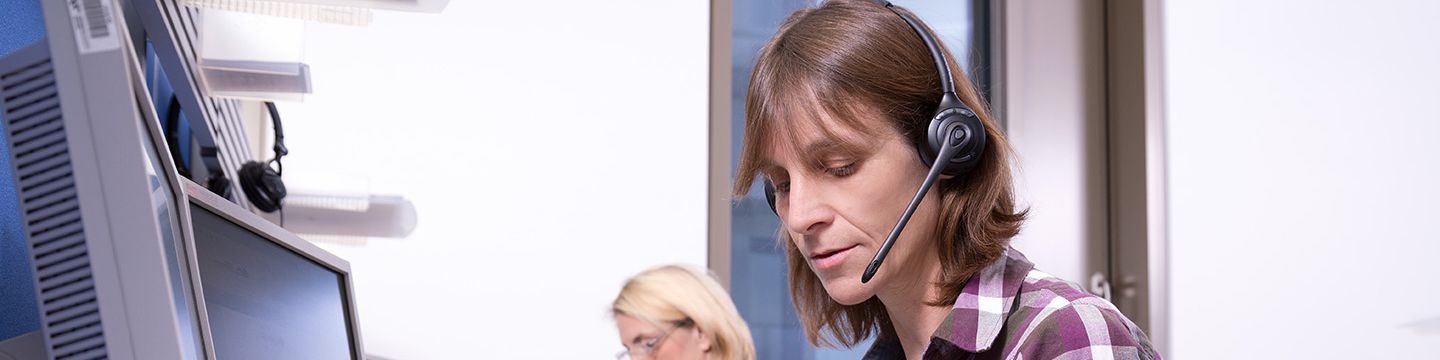Zwei Krebsinformationsdienst-Mitarbeiterinnen arbeiten mit Headset vor einem PC im Telefondienst-Raum