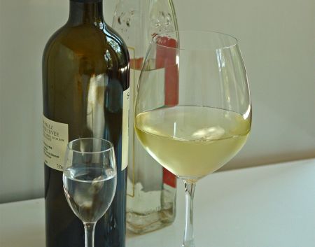 Auf einem Tisch stehen ein gefülltes Glas mit Wein eins gefüllt mit Schnaps neben den Alkoholflaschen.