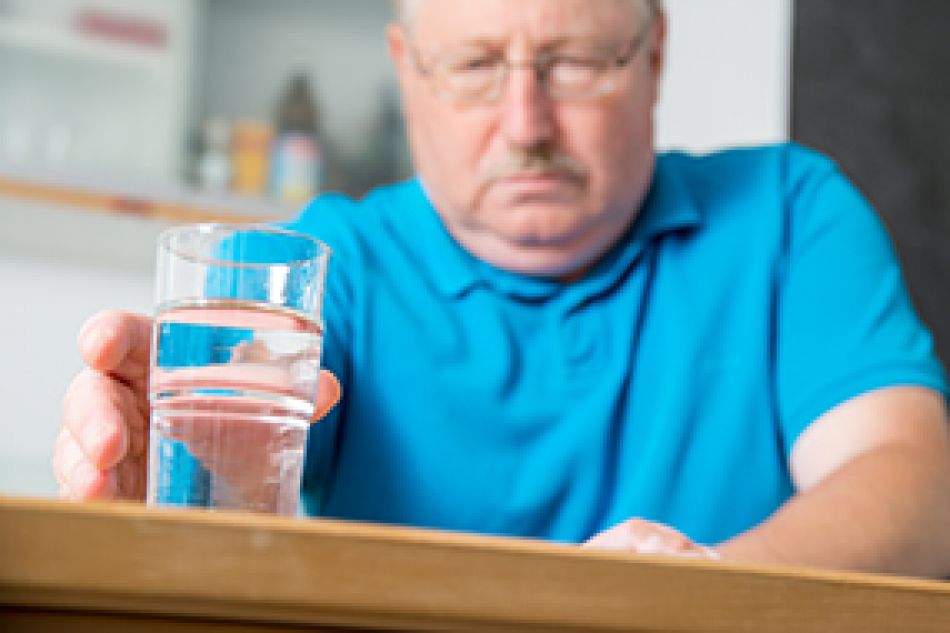 Ein älterer Mann greift nach einem Glas Wasser.  