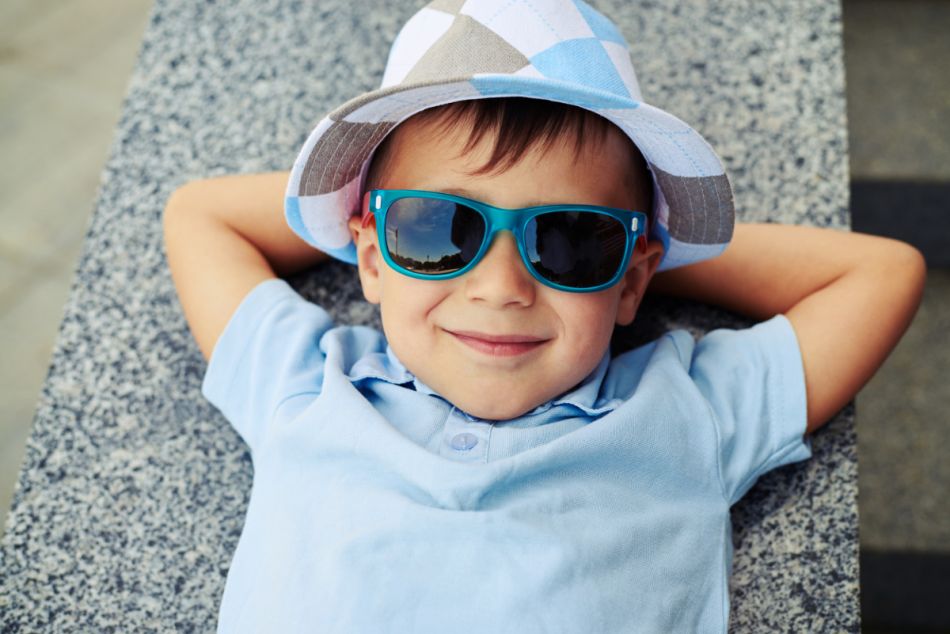Ein kleiner Junge trägt eine Sonnenbrille und einen Hut und schaut in die Kamera.