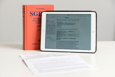 Das Sozialgesetzbuch steht auf einem Tisch, daneben ein Tablet.