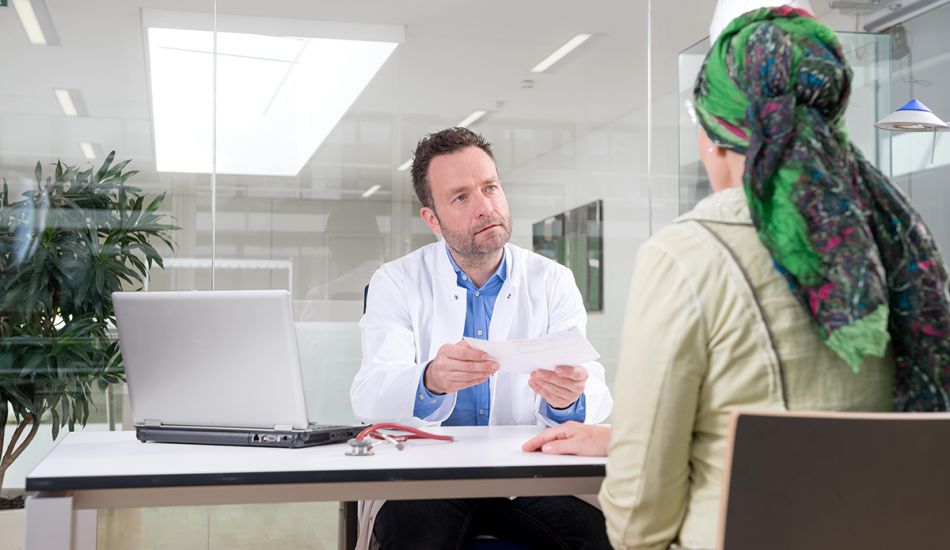 Arzt im Gespräch mit Patientin, die ein Kopftuch trägt.