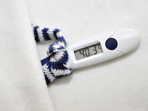 Fieberthermometer, das 40,3 Grad anzeigt, einen winzigen blau-weiß gestreiften Schal trägt und in einem winzigen weißen Bett liegt 