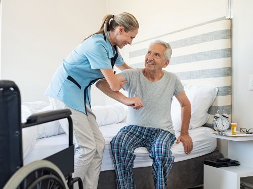 Eine Pflegerin hilft einem Patienten Zuhause am Bett. © Rido, Shutterstock.com