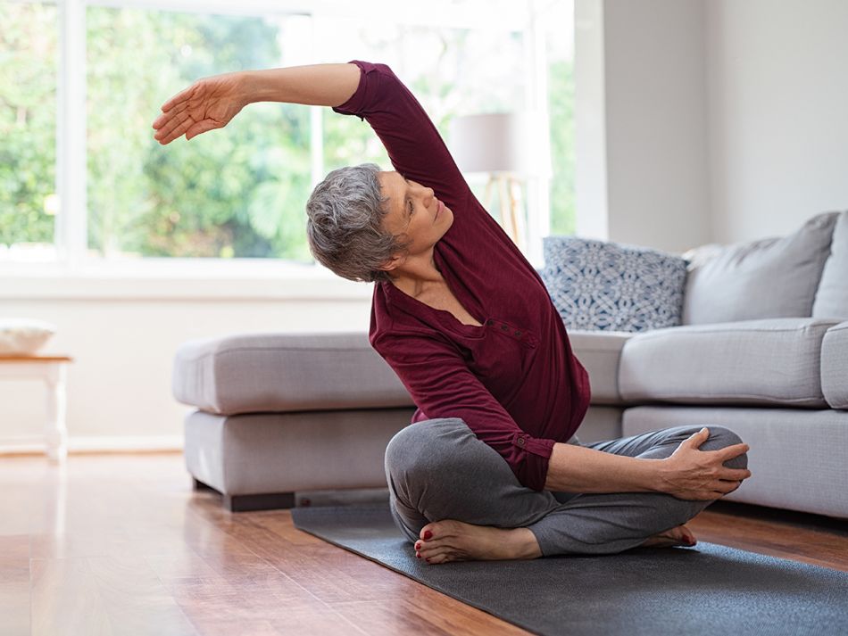 Eine ältere Frau macht Yoga im Wohnzimmer.