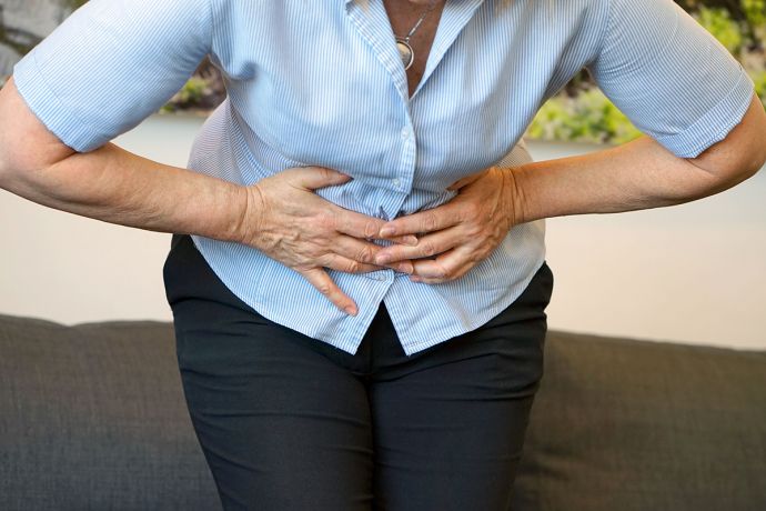 Eine Frau hält sich schmerzgekrümmt die Hände an den Unterleib. © lunopark, Shutterstock