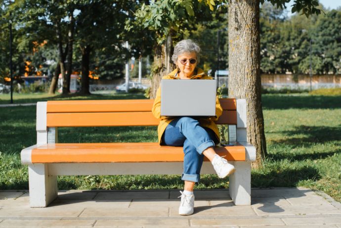 Frau sitzt mit Laptop auf einer Parkbank. 