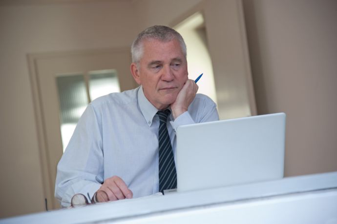 Älterer Mann sitzt nachdenklich vor dem aufgeklappten Laptop