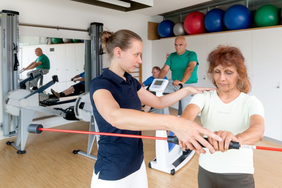 Eine Physiotherapeutin zeigt einer älteren Frau Übungen.