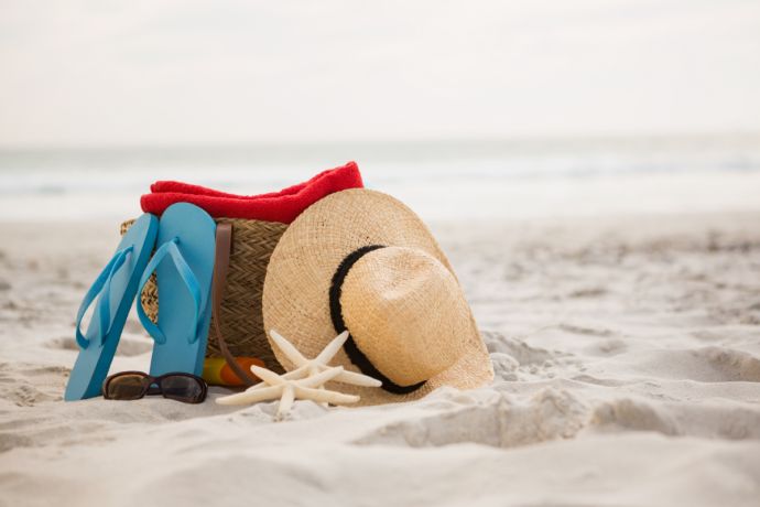 Sonnenhut, Strandtasche, Flip Flops und Sonnenbrille im Sand