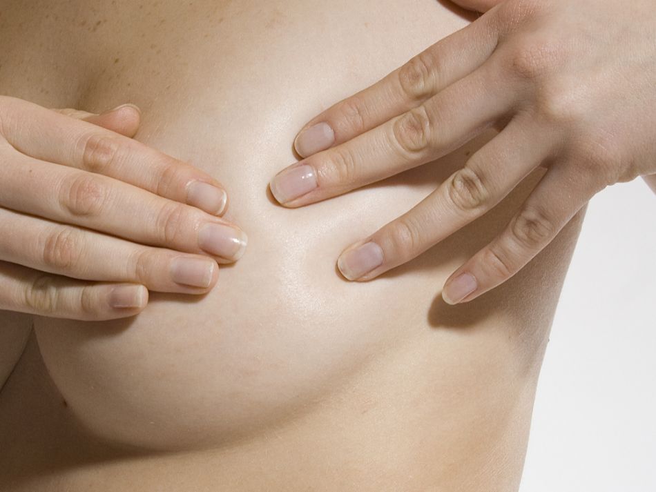Eine Frau tastet sich mit beiden Händen die linke Brust ab, um Brustkrebs früh zu erkennen.