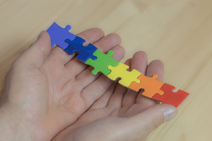 Zwei Hände halten Puzzleteile in Regenbogenfarben.