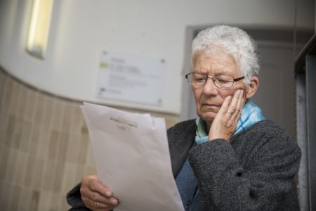 Eine ältere Dame liest ein Schreiben und wirkt erschüttert.