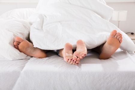 Nackte Füße eines Paares ragen unter der Bettdecke hervor.]