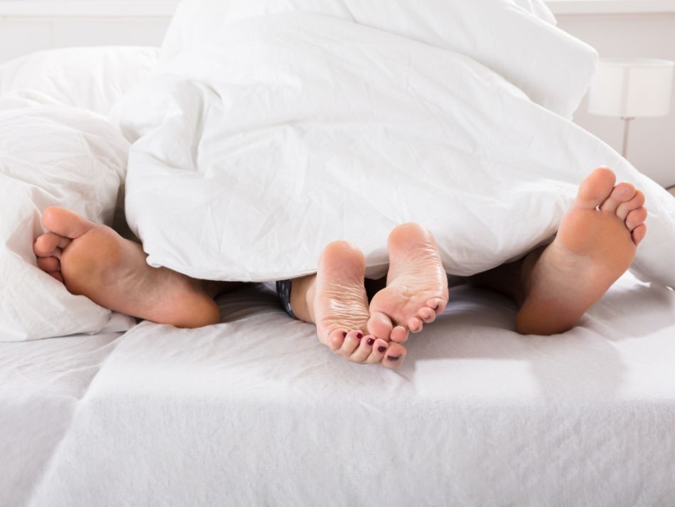 Nackte Füße eines Paares ragen unter der Bettdecke hervor.