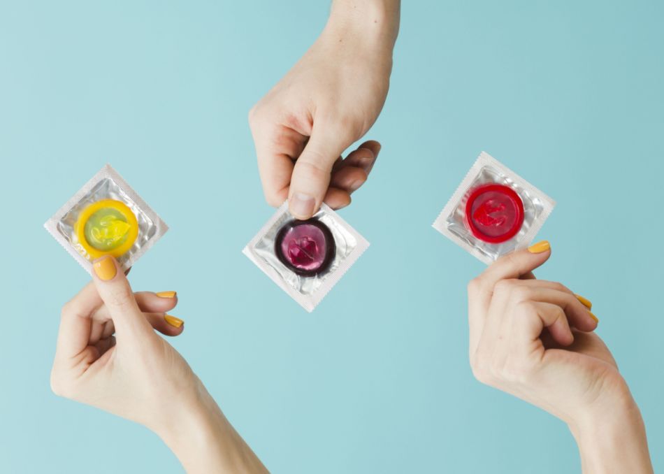 Drei Hände halten drei Kondome – mit Kondomen kann man sich auch beim Oralverkehr vor einer Ansteckung mit HPV schützen.