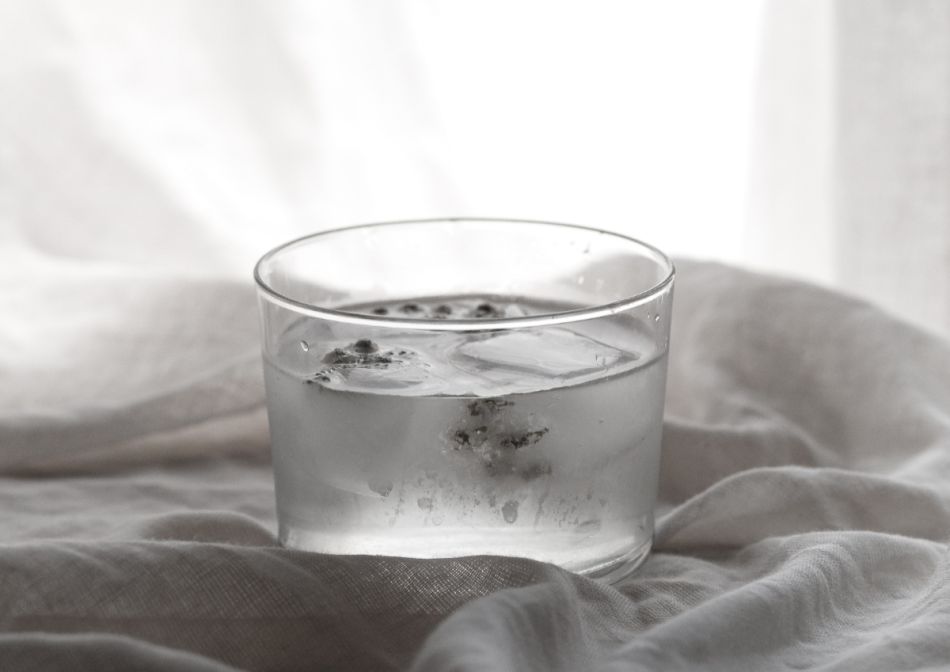 Glas mit Wasser, Eiswürfeln und Kräutern.