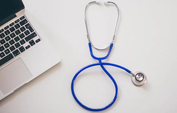 Stethoskop liegt neben aufgeklapptem Laptop