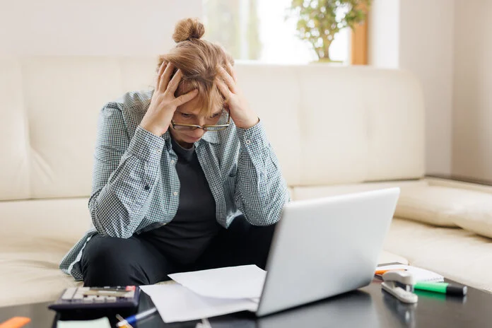 Finanzielle Probleme bei Arbeitsunfähigkeit, © user1236986, Magnific.com Eine Frau sitzt auf dem Sofa und rauft sich ihre Haare. Auf dem Tisch vor ihr stehen ein Labtop und ein Taschenrechner.