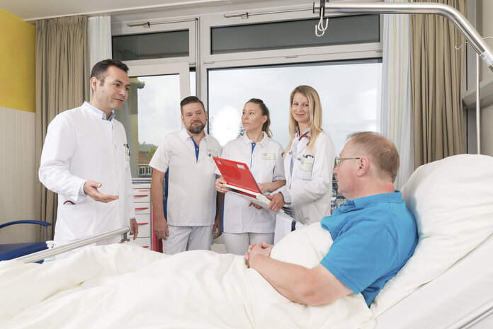 Visite, © Krebsinformationsdienst, DKFZ; Foto: Tobias Schwerdt Arzte und Ärztinnen stehen vor einem Patenten, der im Bett liegt, und halten Visite.