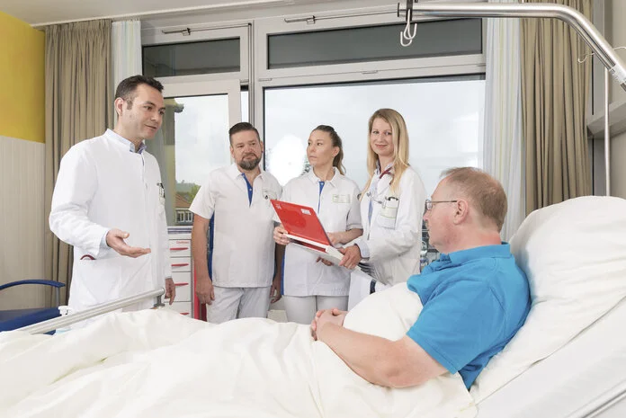 Visite, © Krebsinformationsdienst, DKFZ; Foto: Tobias Schwerdt Arzte und Ärztinnen stehen vor einem Patenten, der im Bett liegt, und halten Visite.