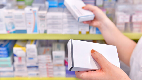Die Hände einer Apotheken-Mitarbeiterin nehmen 2 Arzneimittelpackungen aus dem Apothekenregal