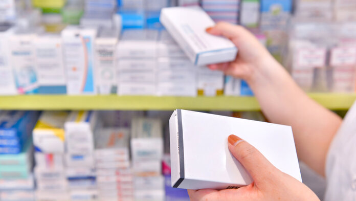 Die Hände einer Apotheken-Mitarbeiterin nehmen 2 Arzneimittelpackungen aus dem Apothekenregal