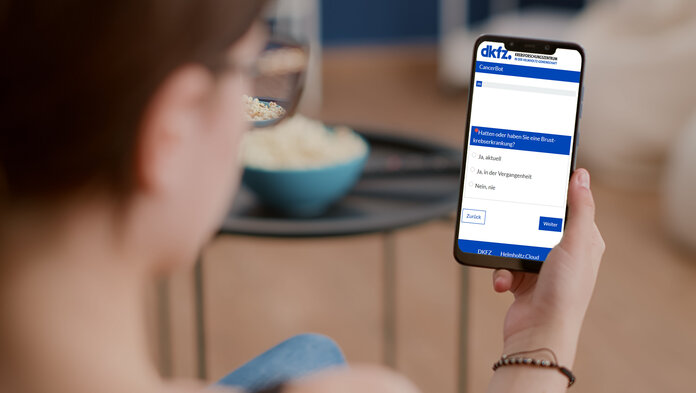 Blickwinkel einer Frau, die auf ihrem Handy die CancerBot-Webseite geöffnet hat. Im Hintergrund verschwommen eine Wohnzimmerszene.