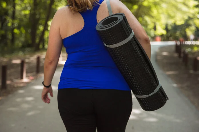 Auf dem Weg zum Sport , © Dobrila Vignjevic, iStock Eine etwas übergewichtige Frau trägt eine Trainingsmatte, von hinten fotografiert