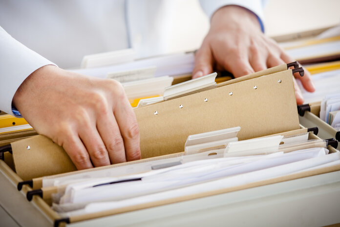 Patientenakte, © TommL, iStock Nahaufnahme von zwei Händen einer Person, die ein Hängeregister aus einer Schublade entnimmt.