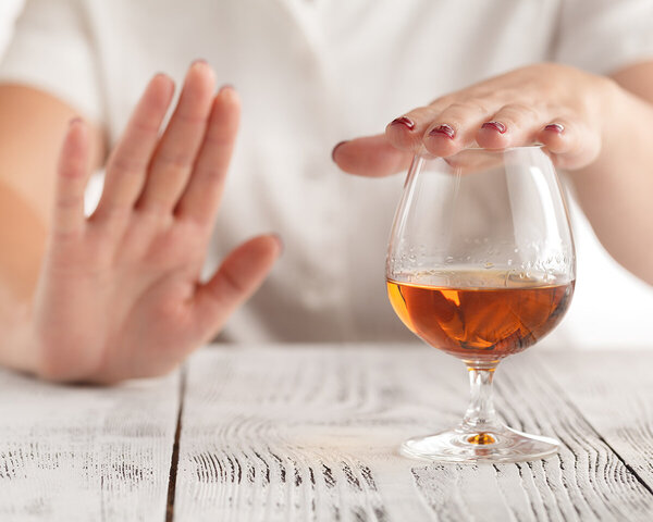 Ein Frau lehnt mit der Hand ein Glas Alkohol ab.