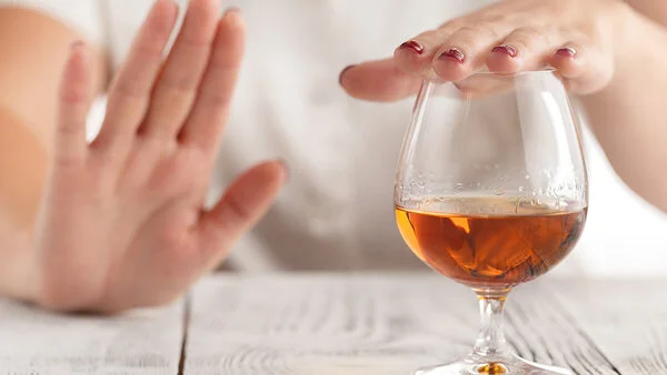 Ein Frau lehnt mit der Hand ein Glas Alkohol ab.