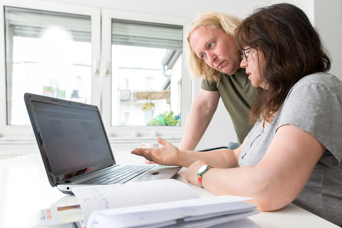 Eine Frau sitzt vor einem Laptop und betrachtet eine Internetseite. Ein Mann neben ihr schaut ebenfalls auf den Bildschirm.