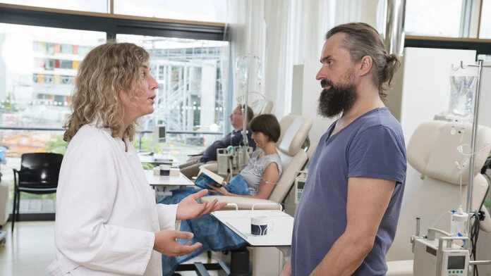 Eine Ärztin steht vor einem Patienten in einer Chemotherapie Ambulanz und spricht.