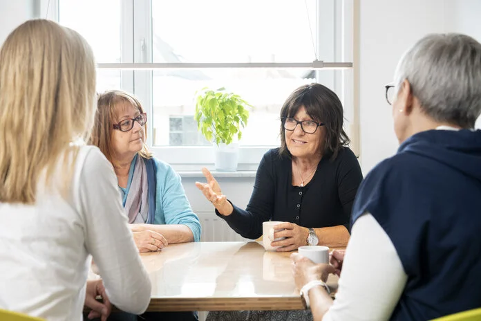 frauen-selbsthilfegruppe-gespraech-am-tisch, © Krebsinformationsdienst, DKFZ; Foto: Tobias Schwerdt 4 Frauen mittleren Alters sitzen zusammen an einem Tisch, trinken Kaffee und reden miteinander. Eine Frau redet, während die anderen 3 zuhören.