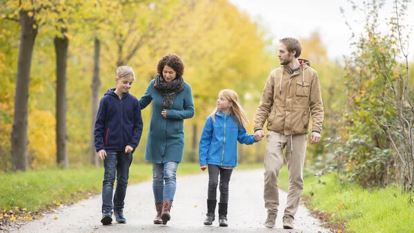 Eine junge Frau und ein junger Mann gehen mit einem Mädchen und einem Jungen im Park spazieren unter unterhalten sich ernst.