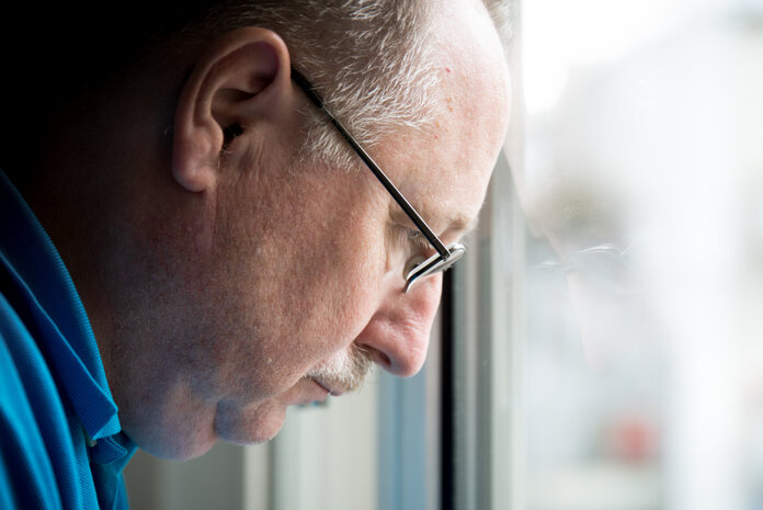 Älterer Mann schaut mit besorgtem Blick aus dem Fenster.