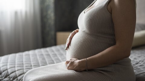 Eine schwangere Frau sitzt auf einem Bett und hält ihren Bauch.