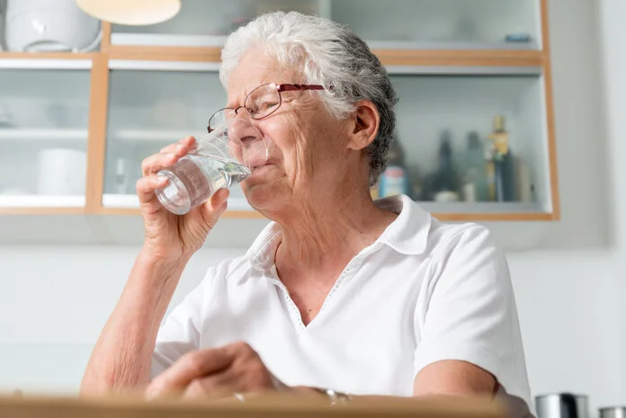 Trinken, © Krebsinformationsdienst, DKFZ; Foto: Tobias Schwerdt Ältere Frau sitzt in der Küche und trinkt Wasser aus einem Glas.