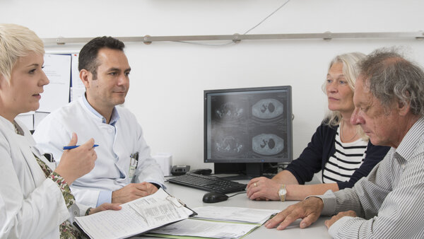 Ein Patient mit Lungenkrebs und seine Angehörige im Gespräch mit zwei Ärzten.