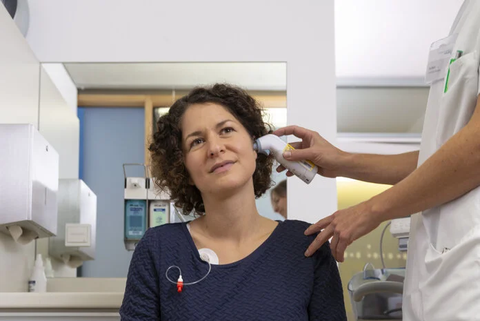 Patientin wird von einer Arzthelferin mit einem Infrarot-Thermometer Fieber gemessen.